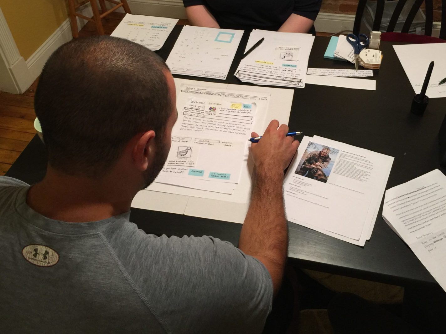 A white male waterfowl hunter facing away from the camera, looking at and interacting with a paper prototype of our design